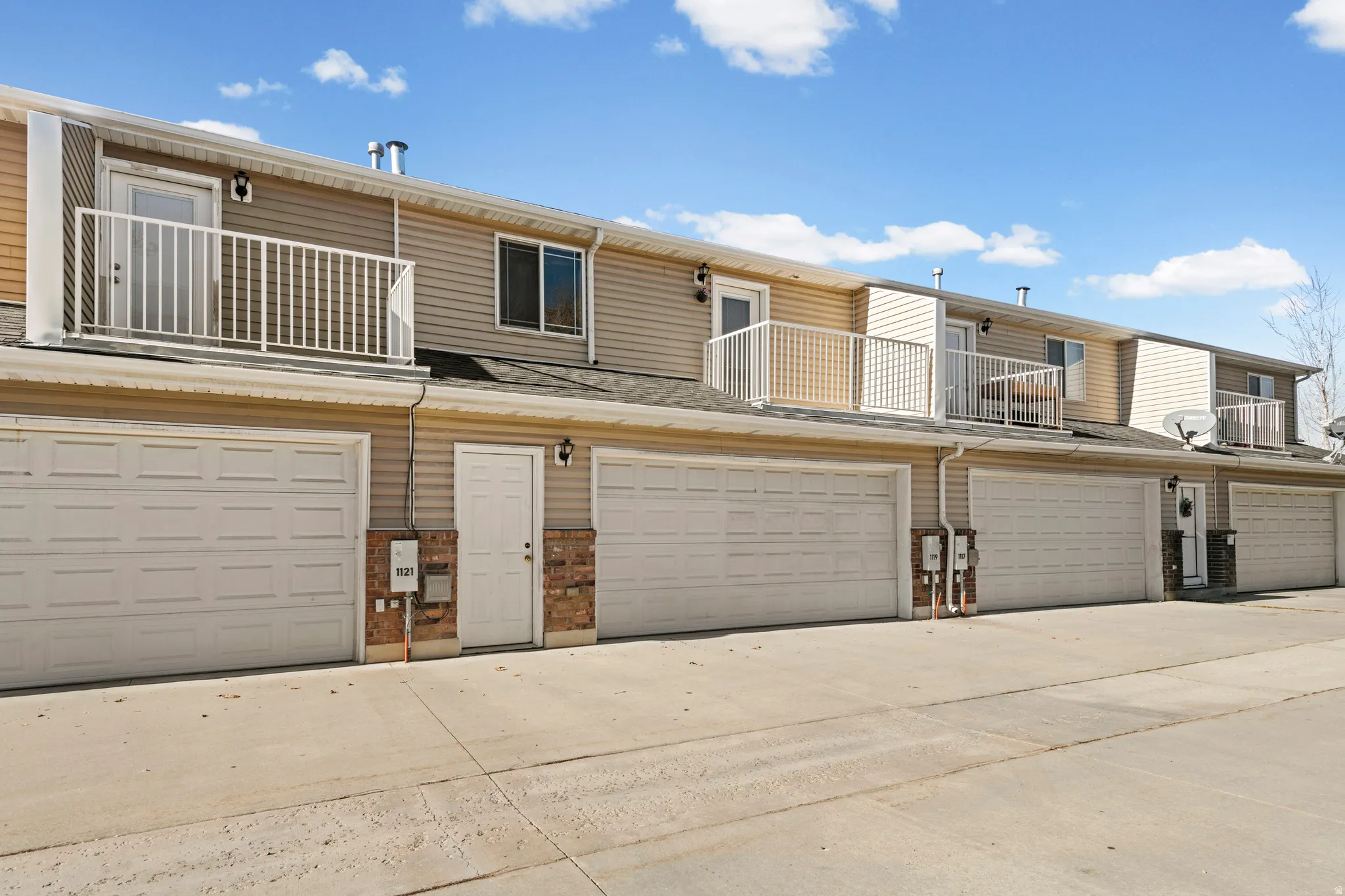 Back of property with a balcony, brick siding, driveway, and a garage