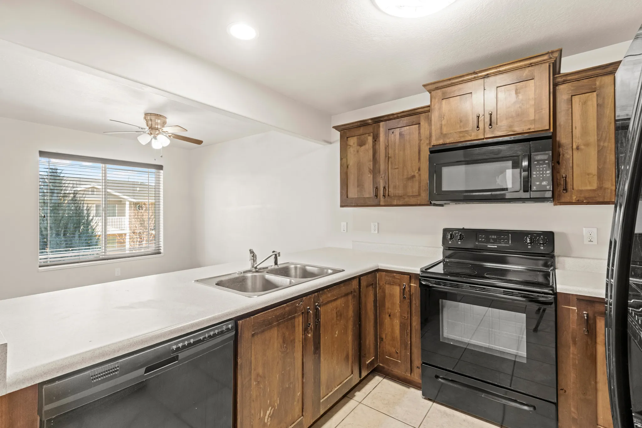 Kitchen with black appliances, light countertops, light tile patterned floors, ceiling fan, and wood finish cabinetry