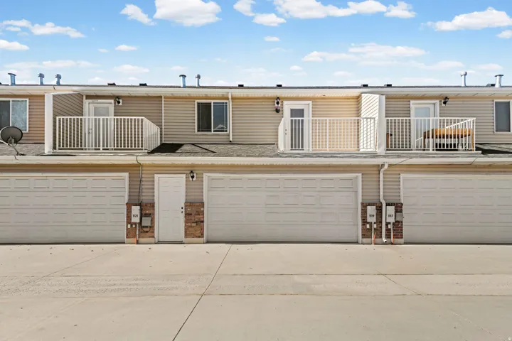 Back of property featuring a balcony, driveway, a garage, and brick siding
