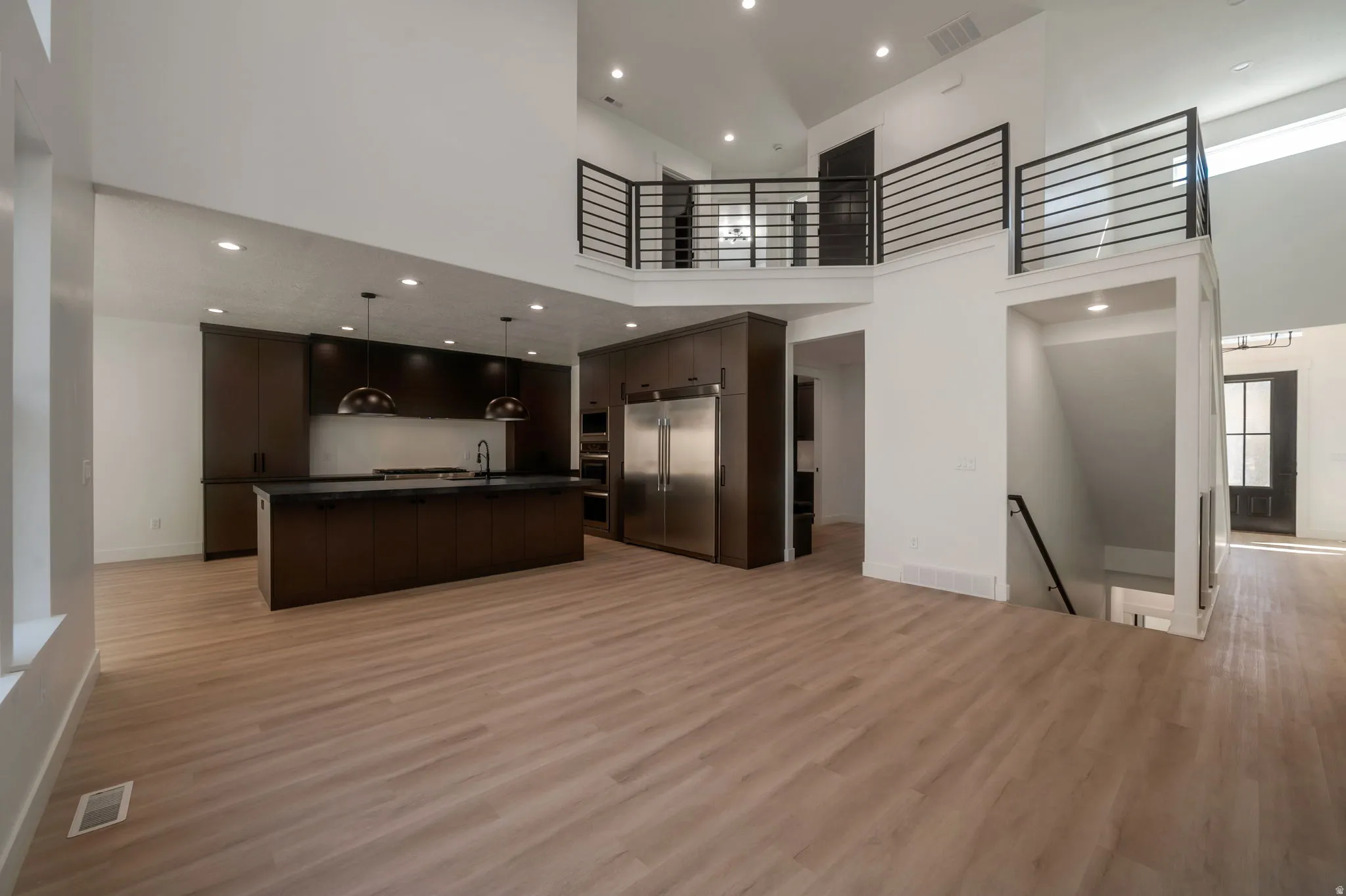Kitchen featuring dark wood finish cabinets, a kitchen island with sink, stainless steel built in refrigerator, dark countertops, and light wood-type flooring