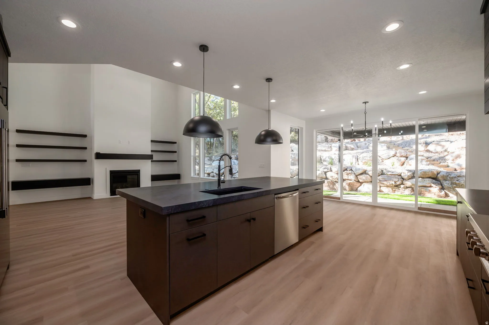 Kitchen with dark countertops, a center island with sink, light wood-style floors, and a glass covered fireplace