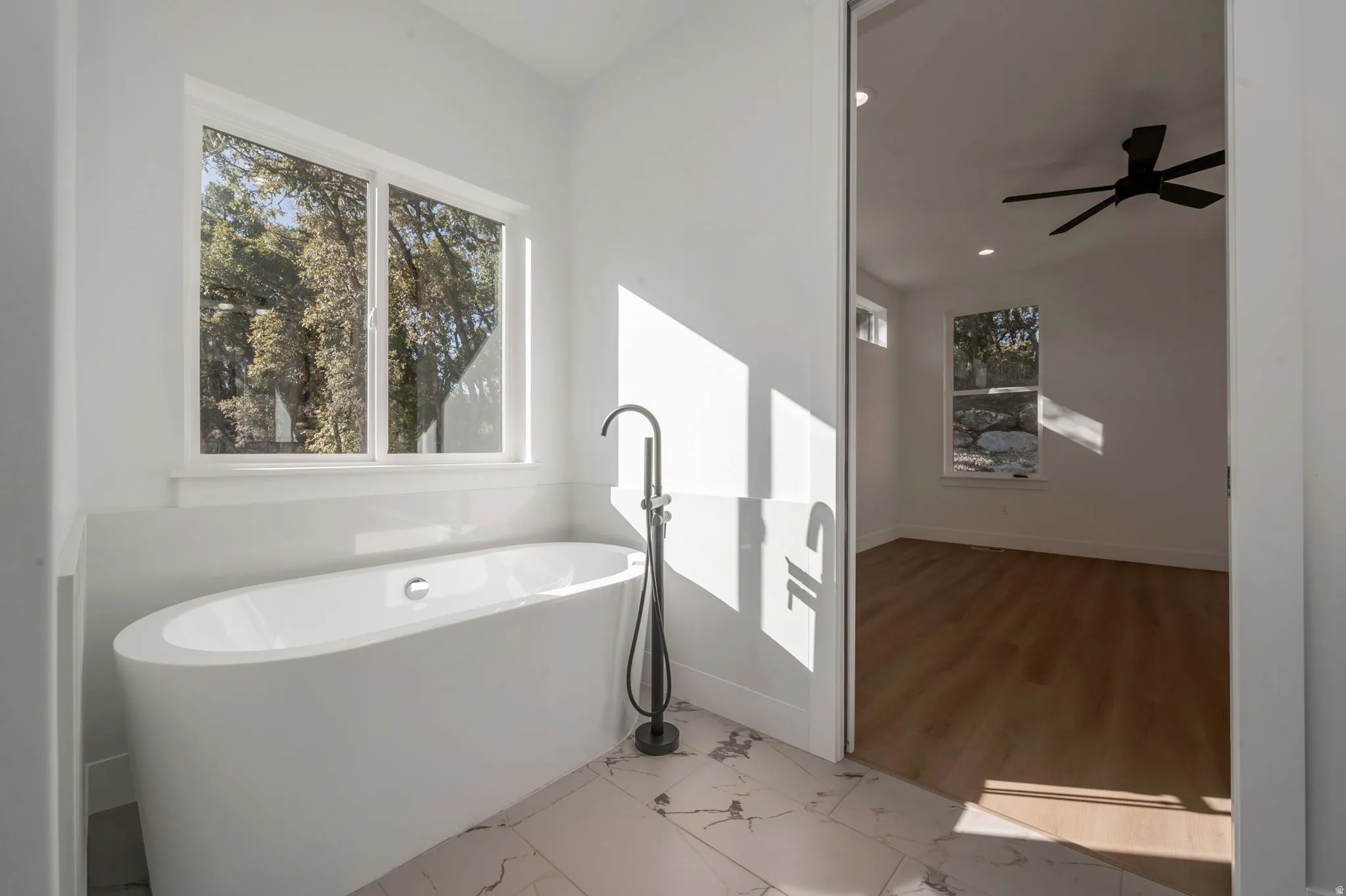 Full bath with a freestanding tub, light marble finish floors, and ceiling fan