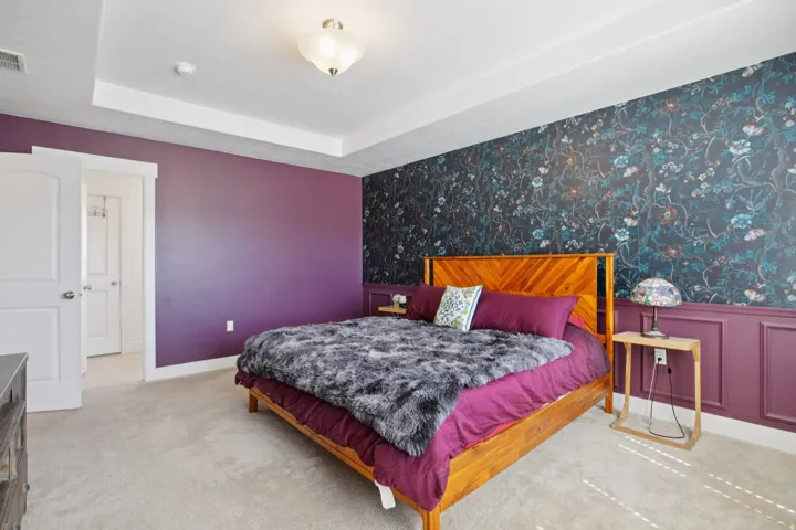 Bedroom featuring wallpapered walls, an accent wall, light colored carpet, and a raised ceiling