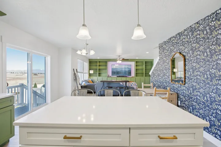 Two tone kitchen with built in features, light stone counters, two tone cabinetry, wallpapered walls, and a kitchen island