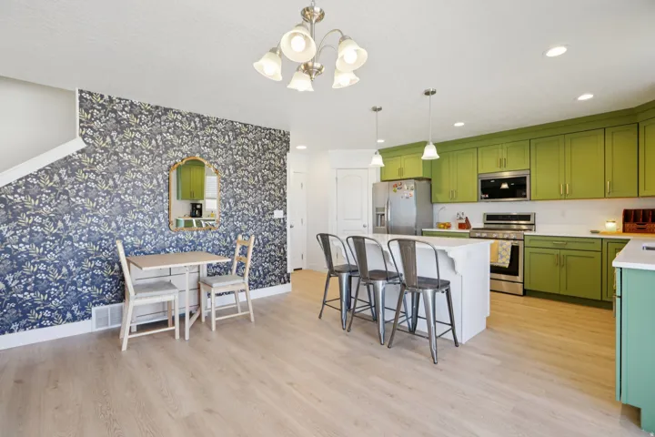 Two tone kitchen featuring wallpapered walls, stainless steel appliances, light wood-style flooring, a breakfast bar area, and light stone counters