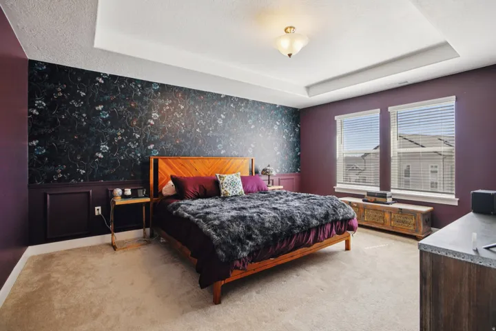 Bedroom with wallpapered walls, a raised ceiling, light colored carpet, an accent wall, and a textured ceiling