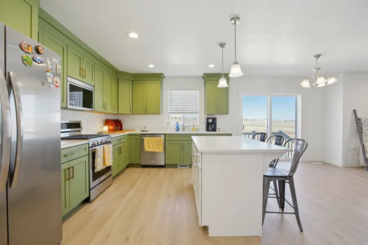 Kitchen featuring green cabinetry, stainless steel appliances, light wood-type flooring, a kitchen bar, and a textured ceiling