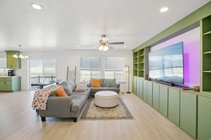 Living area with light wood-type flooring, ceiling fan, built in features, hanging lights, and a textured ceiling