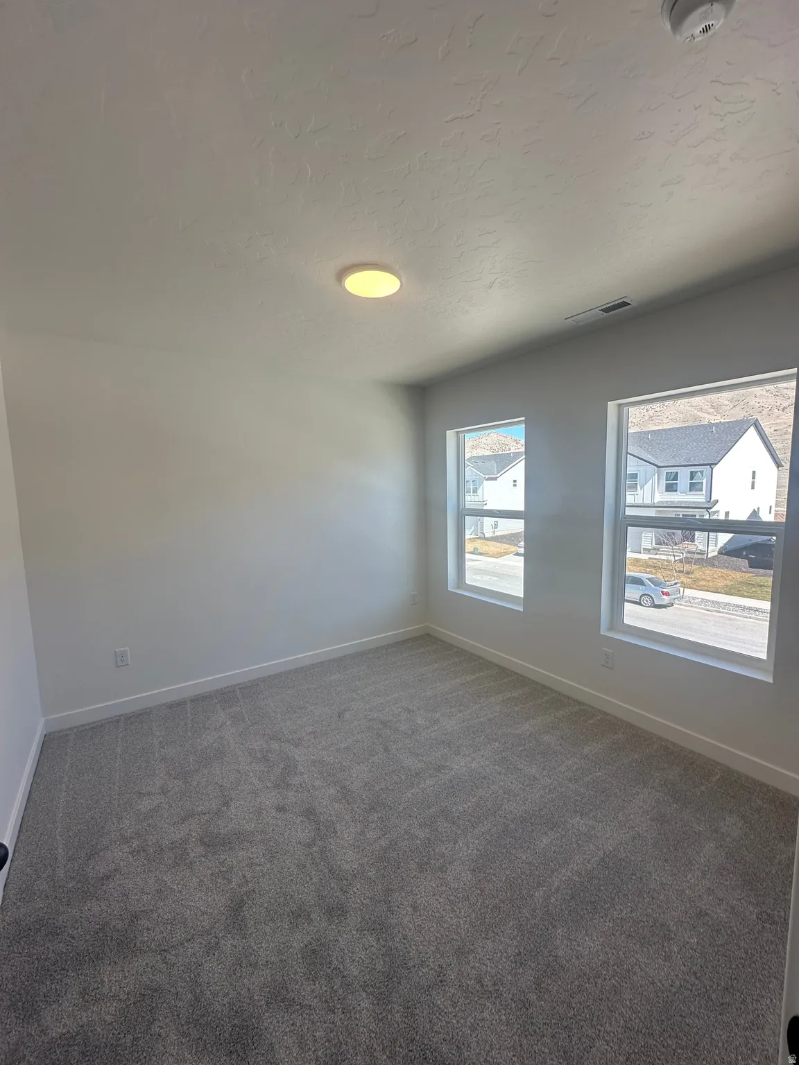 Empty room featuring dark carpet, a textured ceiling, and a smoke detector
