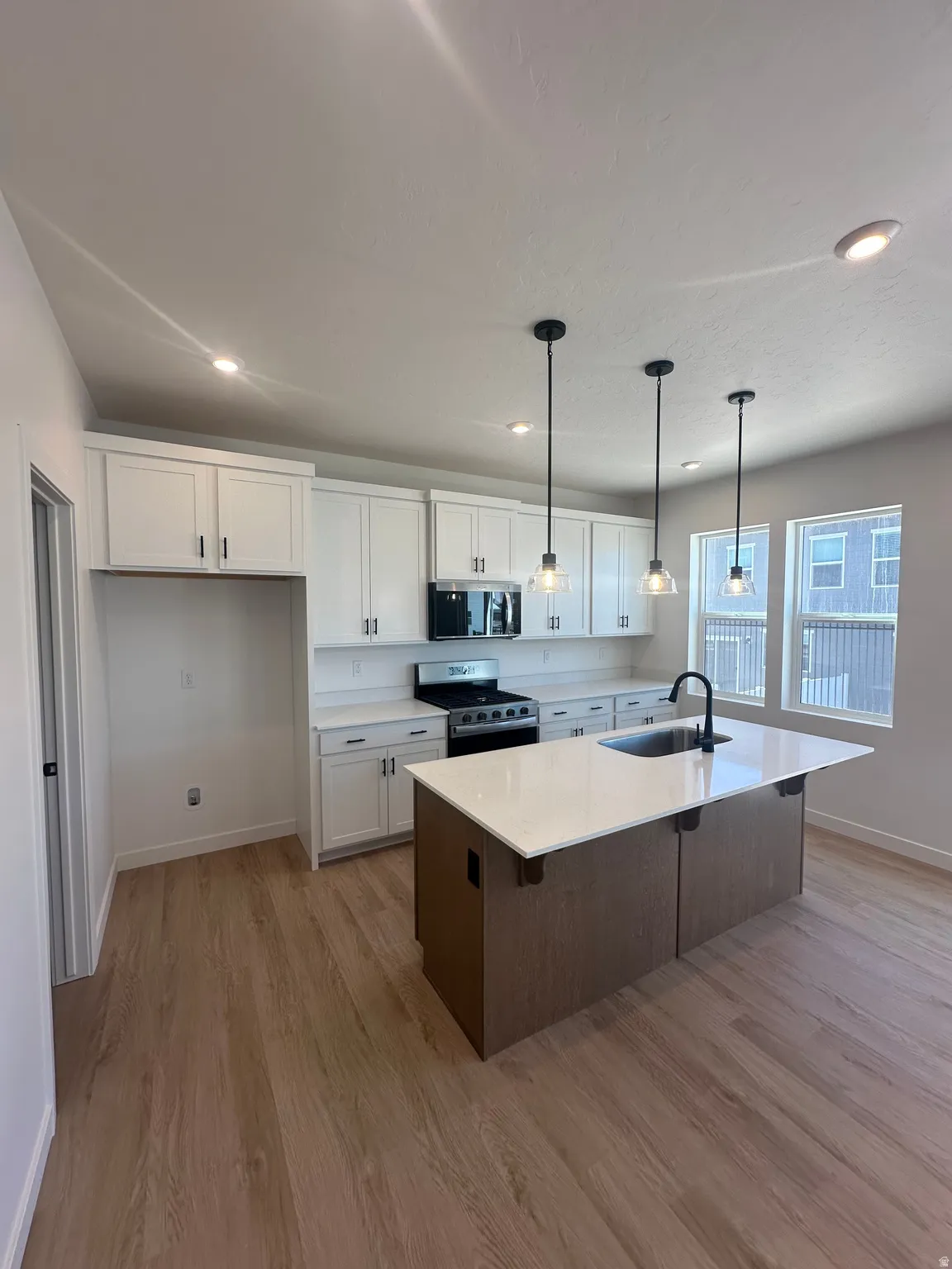 Kitchen featuring two tone cabinets, stainless steel appliances, hanging light fixtures, light wood-style flooring, and an island with sink