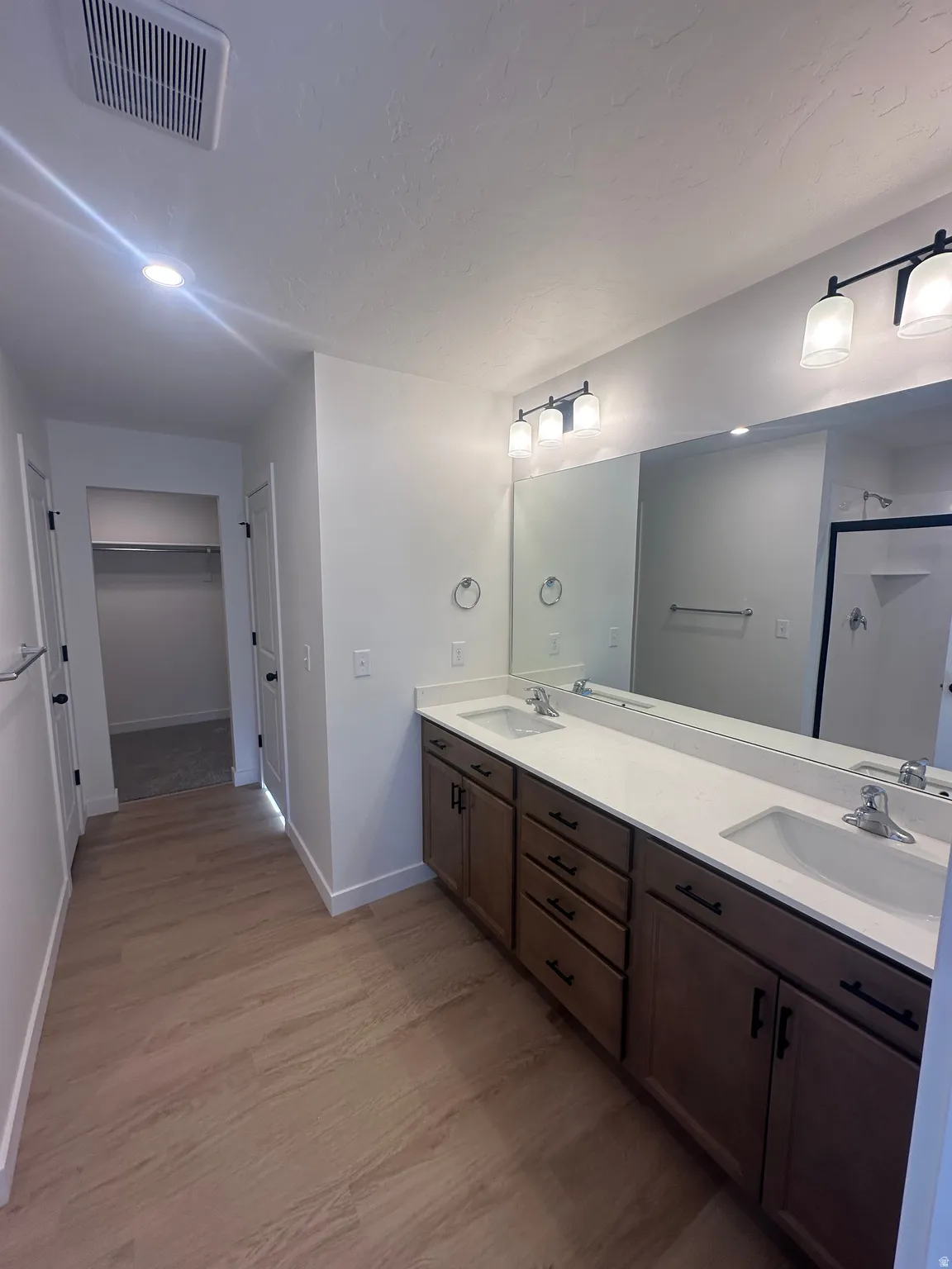 Bathroom featuring double vanity, light wood-style flooring, a stall shower, and a spacious closet