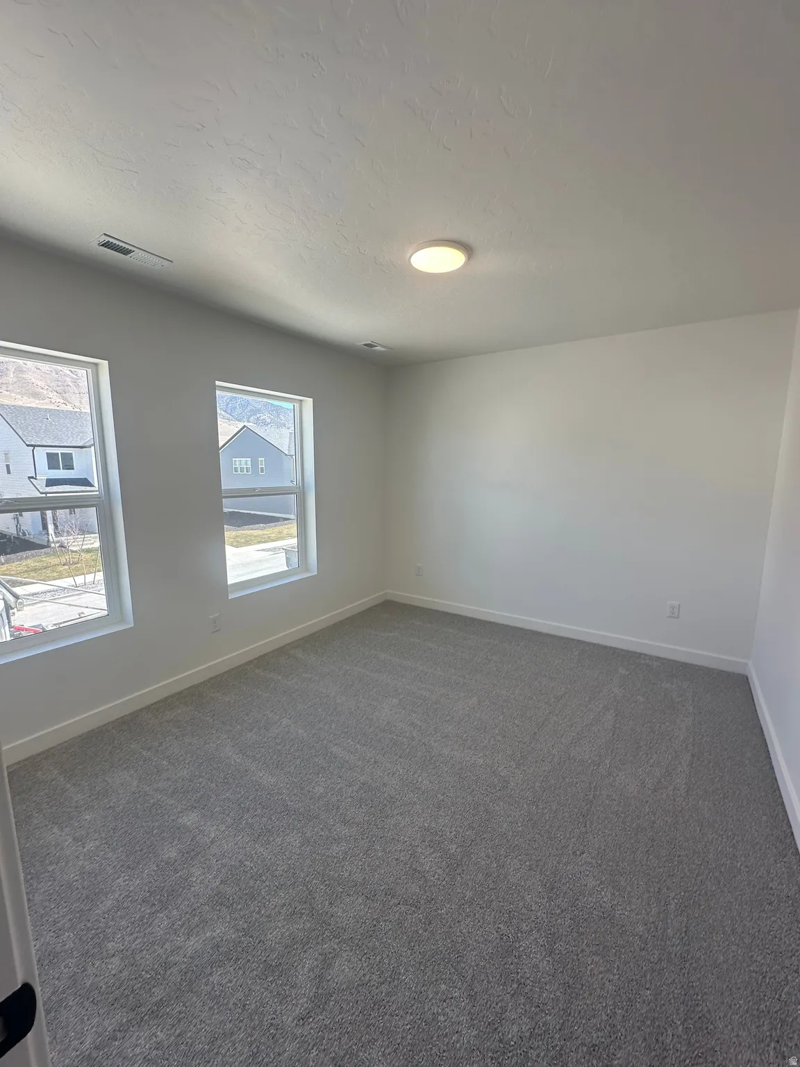 Unfurnished room featuring dark carpet, plenty of natural light, and a textured ceiling