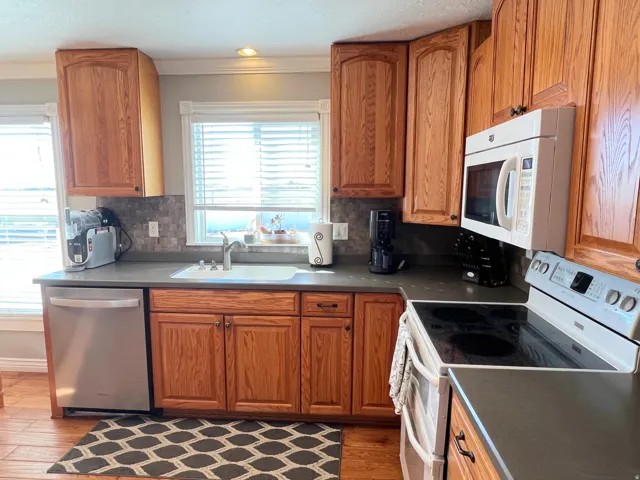 Kitchen with white appliances, dark countertops, wood finish cabinets, wood finished floors, and crown molding