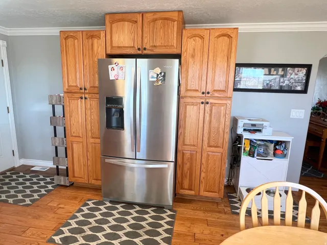 Kitchen featuring crown molding, stainless steel fridge, light wood finished floors, wood finish cabinetry, and a textured ceiling