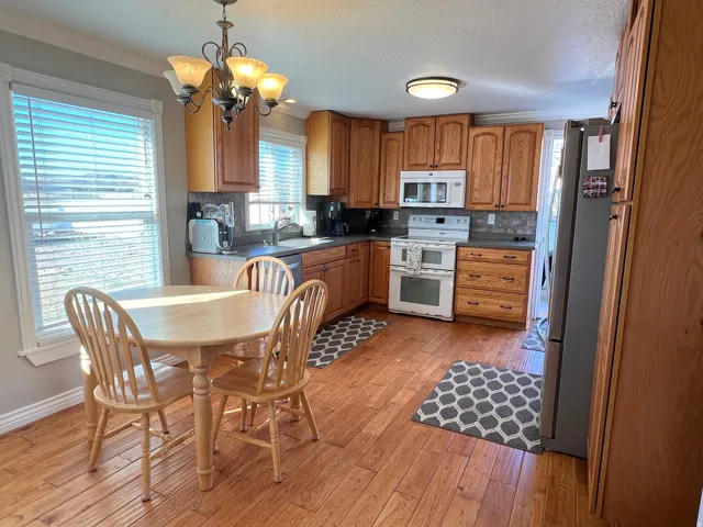 Kitchen featuring wood finish cabinetry, dark countertops, stainless steel and white appliances, hanging dining light, and light wood-style floors