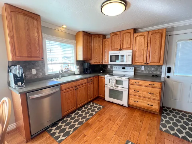 Kitchen featuring dark countertops, white appliances, wood finish cabinetry, light wood-style floors, and ornamental molding