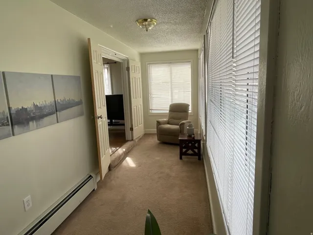 Corridor with a baseboard heating unit, carpet floors, and a textured ceiling