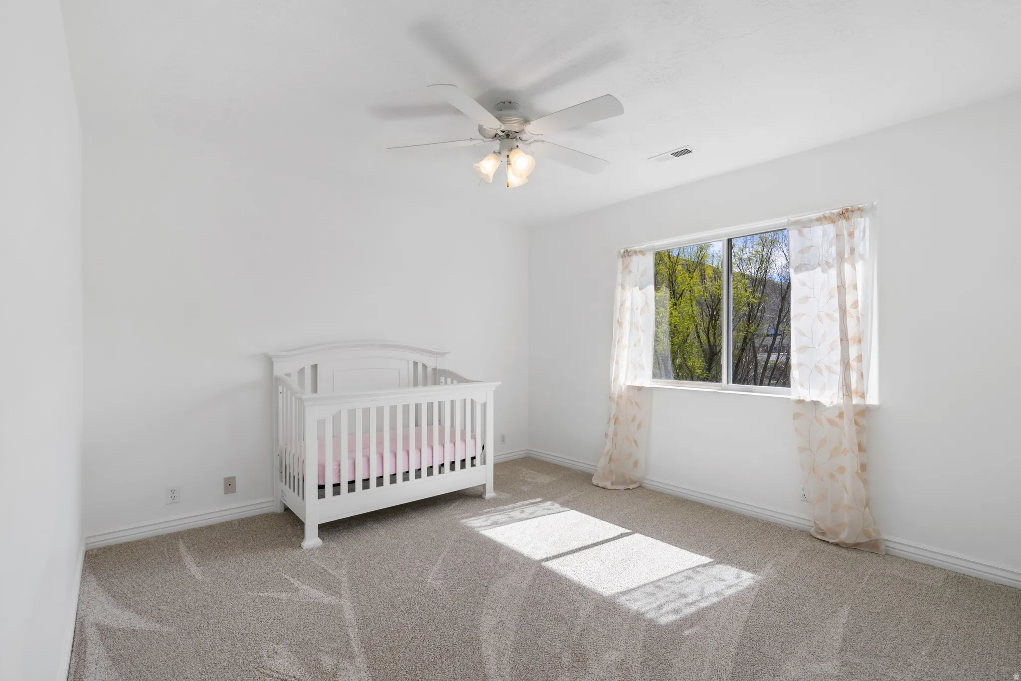 Carpeted bedroom with a crib and ceiling fan