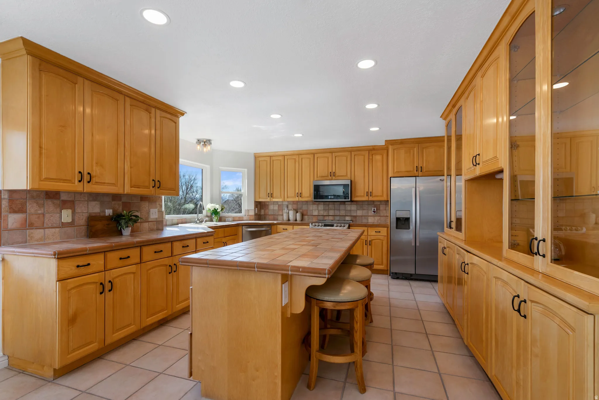 Kitchen featuring tile countertops, a kitchen bar, stainless steel appliances, light tile patterned floors, and a kitchen island