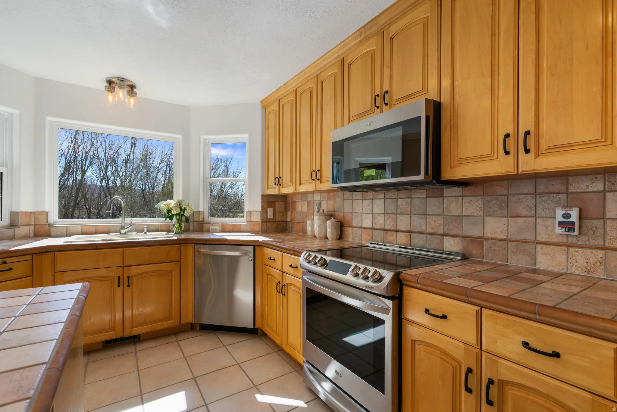 Kitchen with tile countertops, stainless steel appliances, light tile patterned floors, and tasteful backsplash