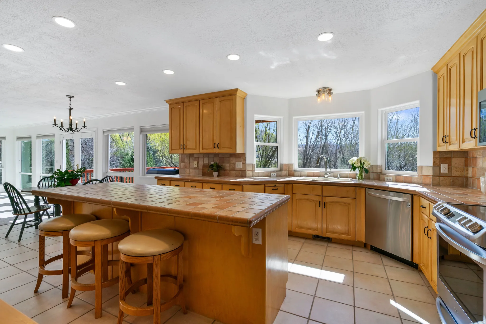 Kitchen featuring tile countertops, stainless steel appliances, hanging lights, a breakfast bar area, and light tile patterned flooring