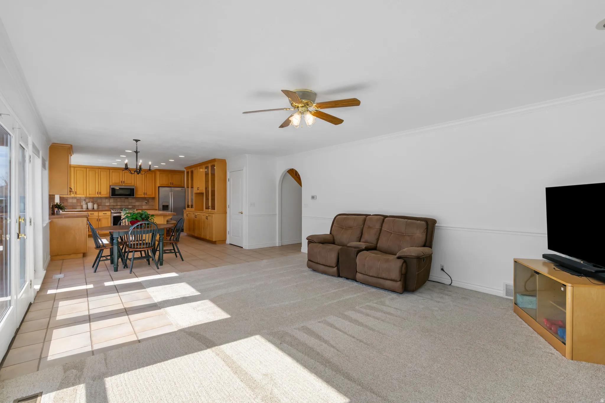 Living room featuring light tile patterned floors, crown molding, arched walkways, a chandelier, and light carpet