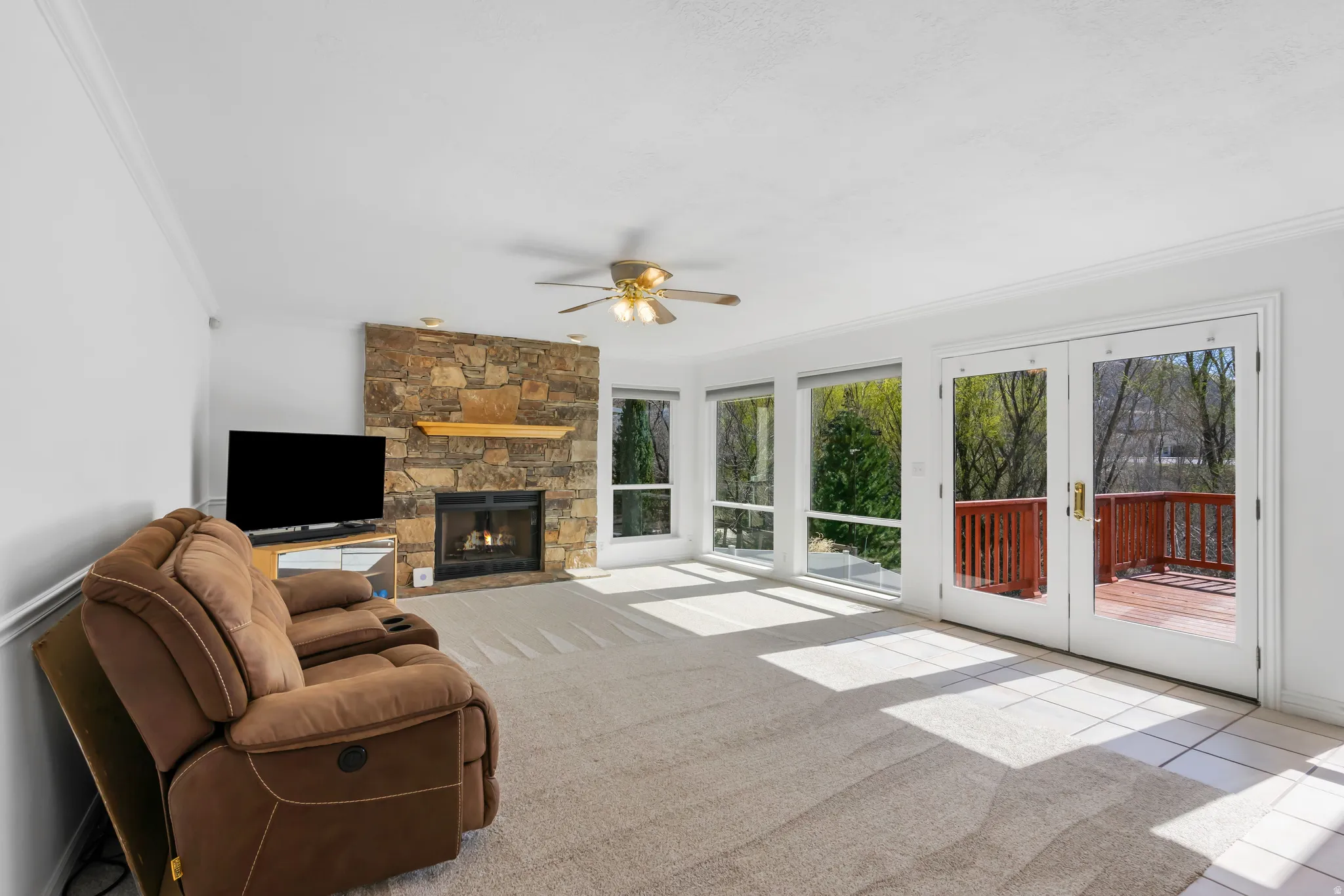 Living room featuring french doors, a stone fireplace, ornamental molding, ceiling fan, and light colored carpet