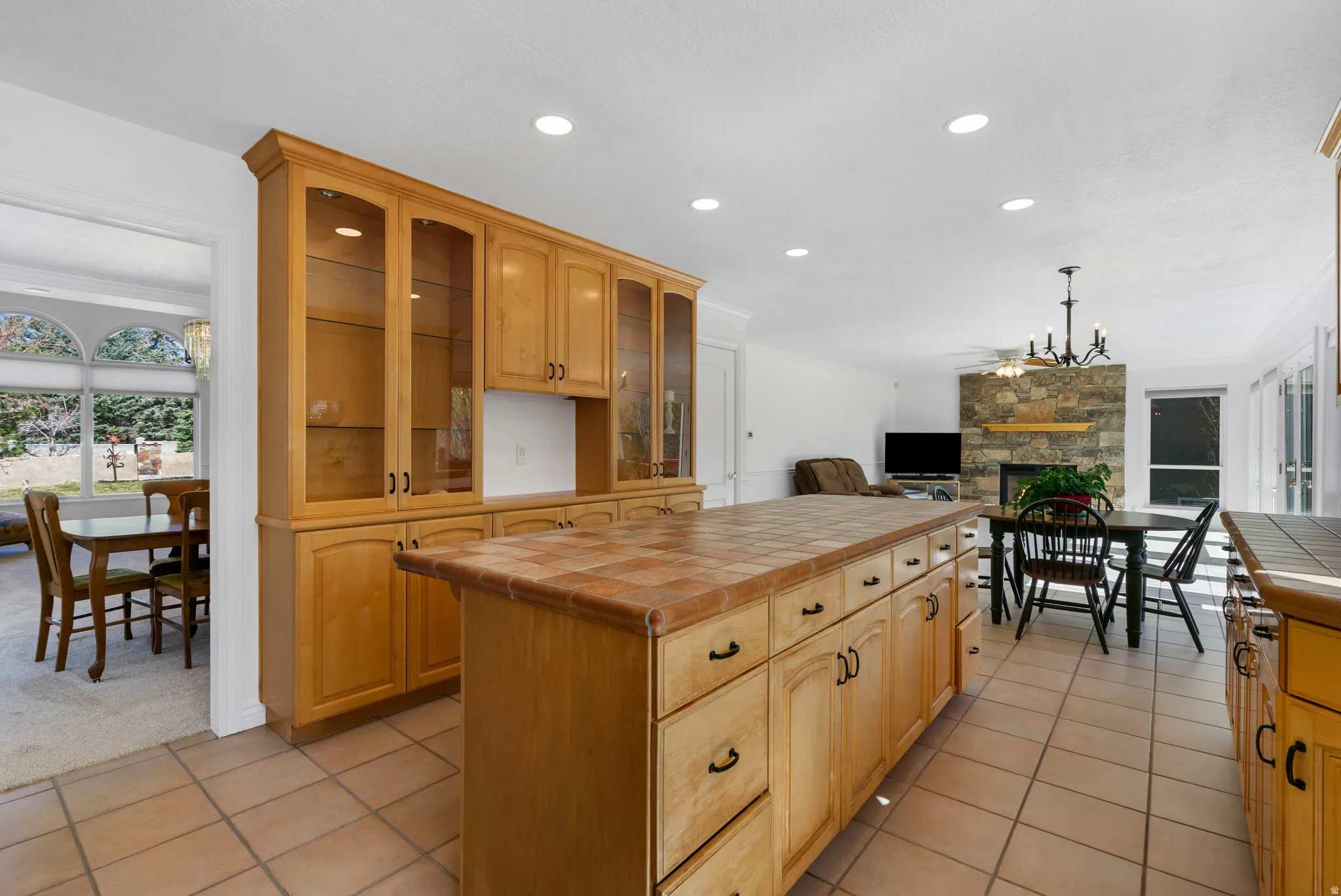 Kitchen with tile counters, glass insert cabinets, decorative light fixtures, open floor plan, and a fireplace