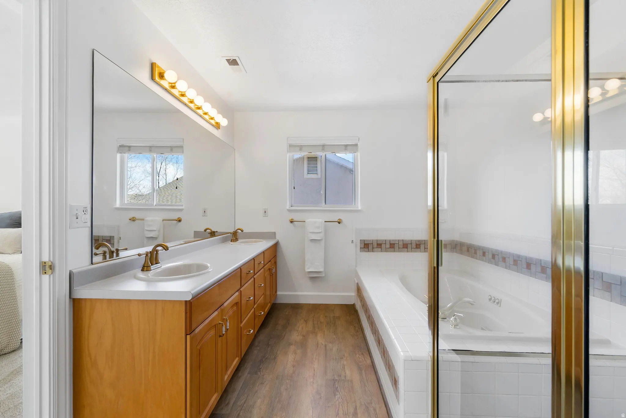 Bathroom with double vanity, dark wood-style flooring, and a garden tub