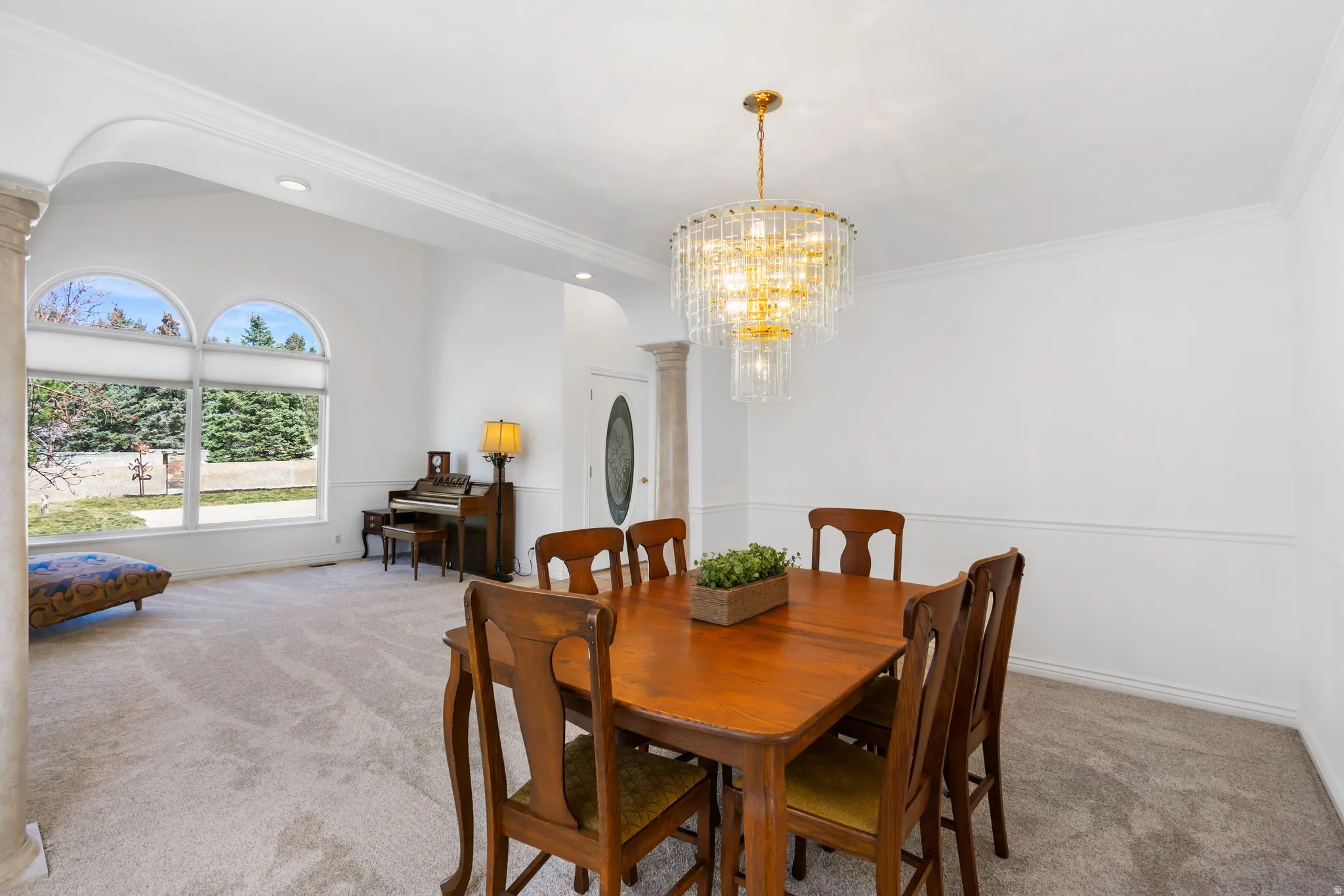 Dining space with light colored carpet, arched walkways, suspended lighting, and ornamental molding