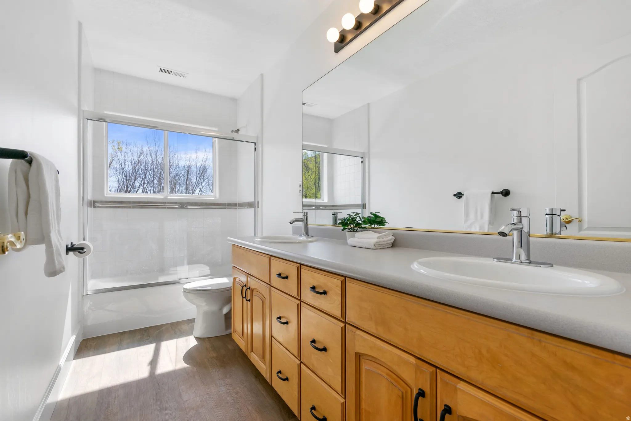 Bathroom with double vanity, combined bath / shower with glass door, and dark wood-style flooring