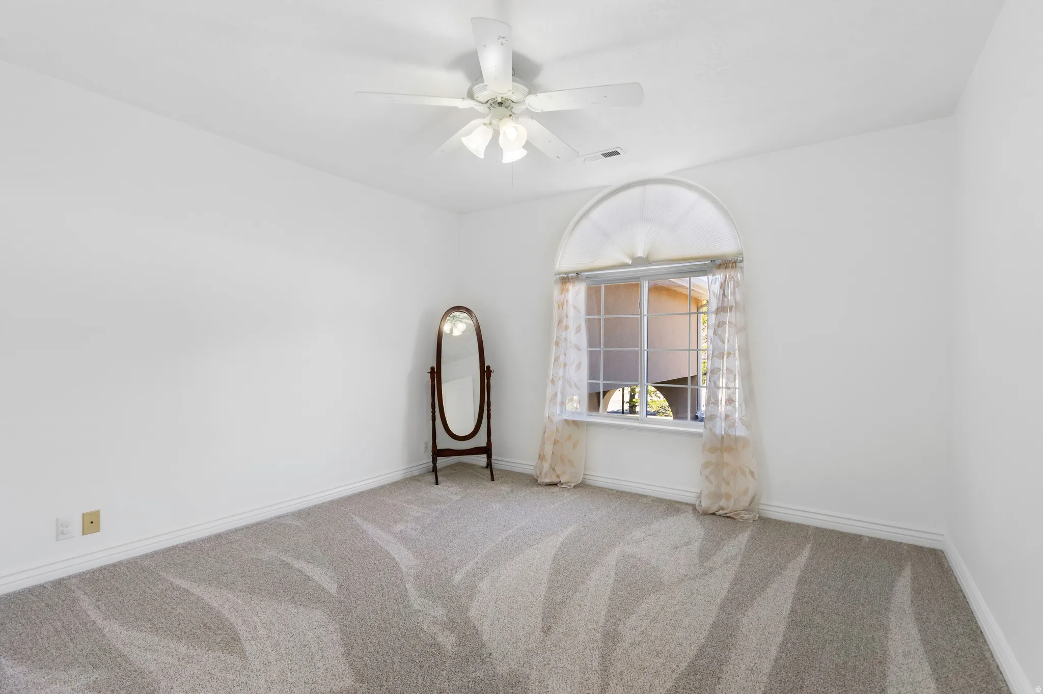 Empty room with light carpet and a ceiling fan