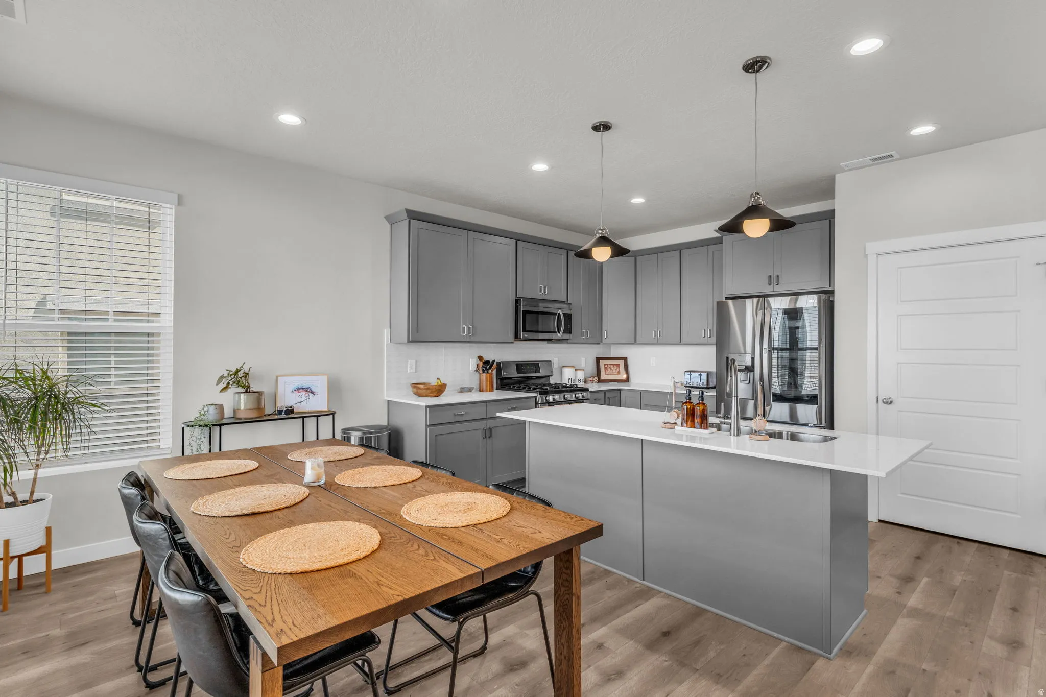 Kitchen with gray cabinetry, a center island with sink, stainless steel appliances, pendant lighting, and light wood-type flooring