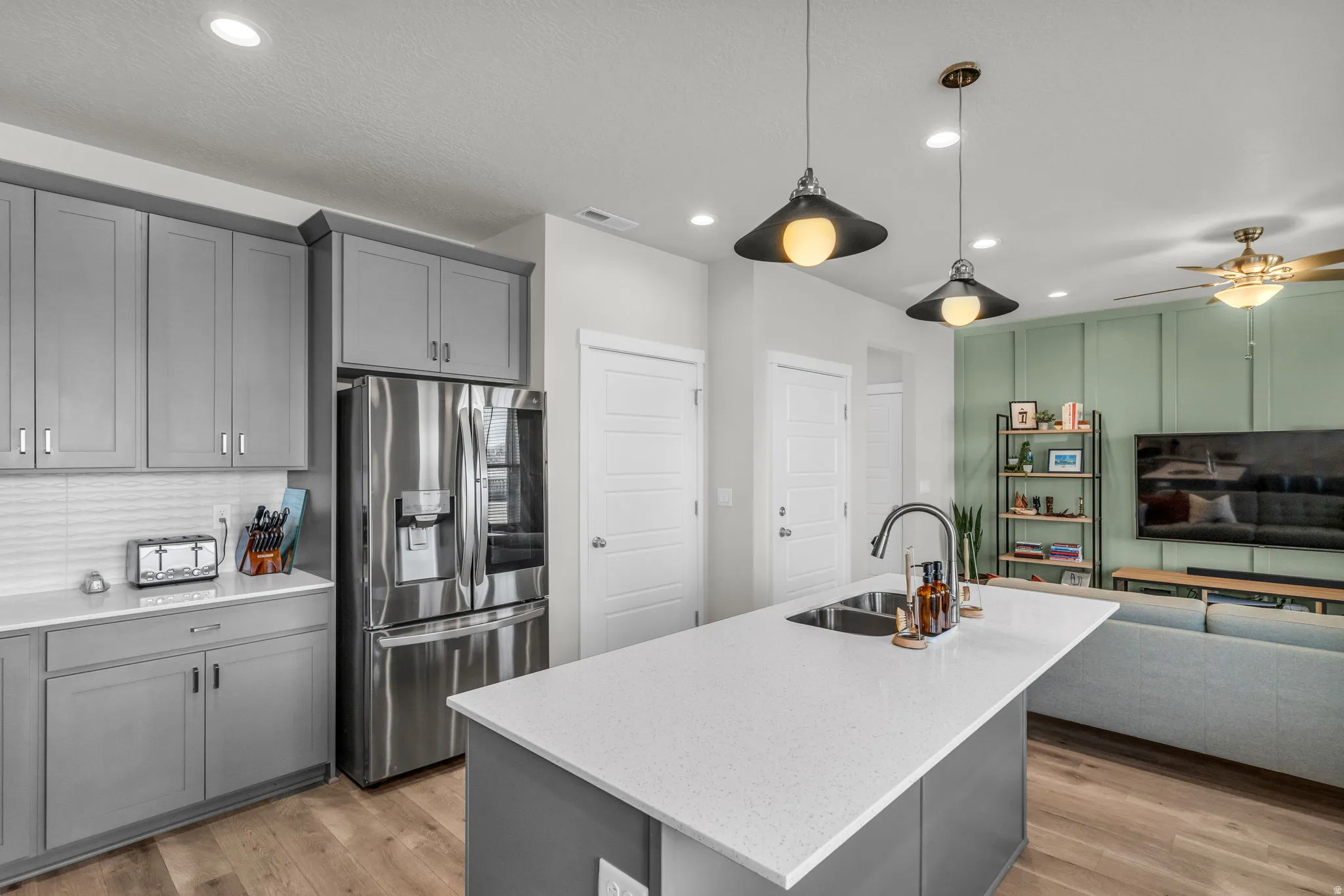 Kitchen with gray cabinets, open floor plan, stainless steel fridge with ice dispenser, light wood-style flooring, and an island with sink