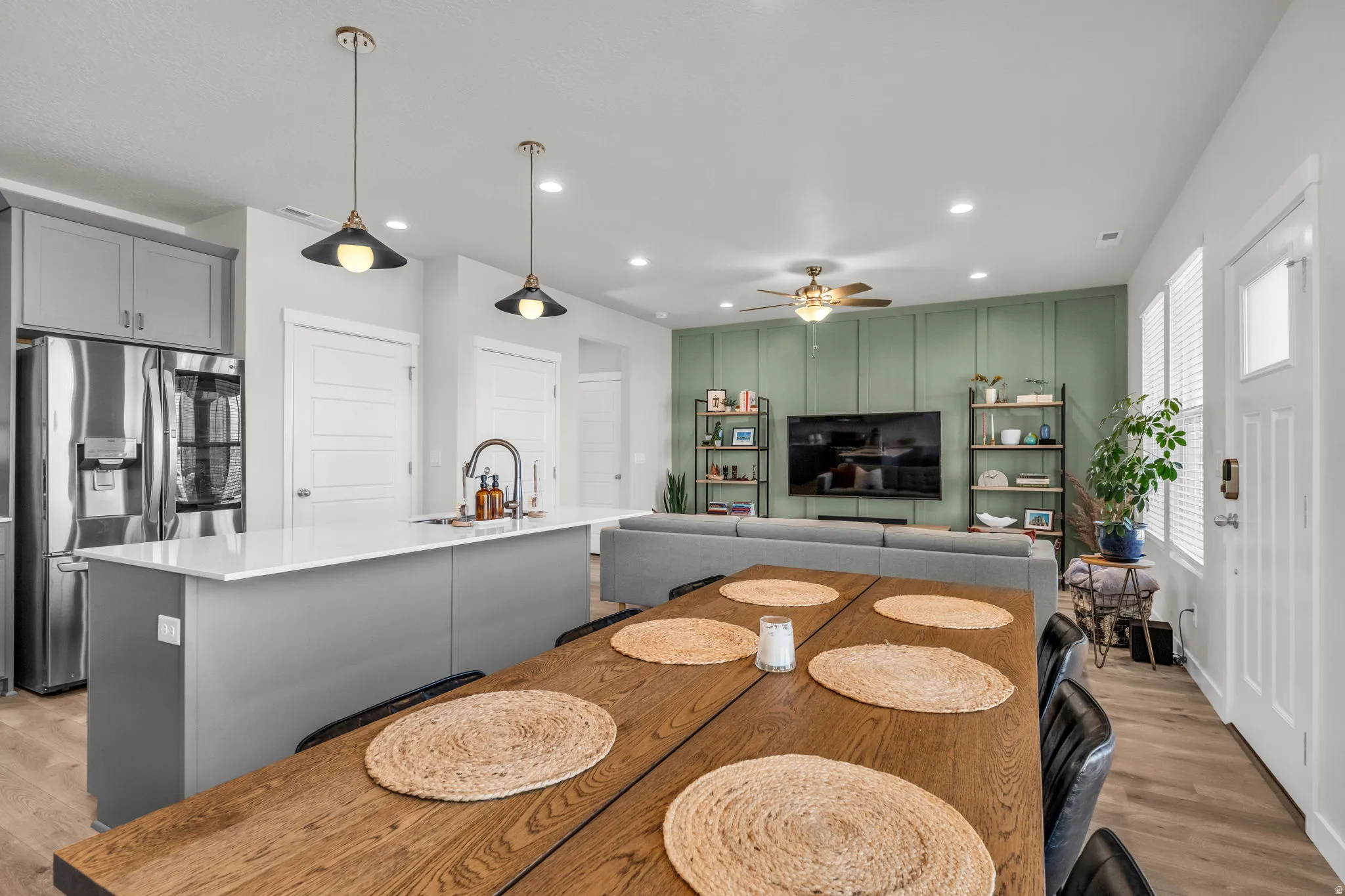 Kitchen with gray cabinets, light wood finished floors, stainless steel refrigerator with ice dispenser, open floor plan, and a kitchen island with sink