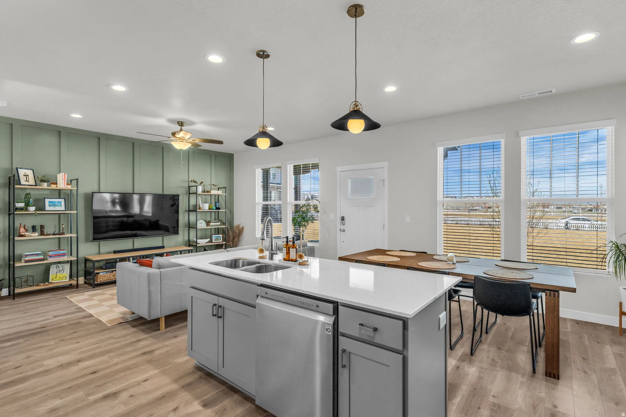 Kitchen featuring dishwasher, light wood-type flooring, a center island with sink, pendant lighting, and light stone counters