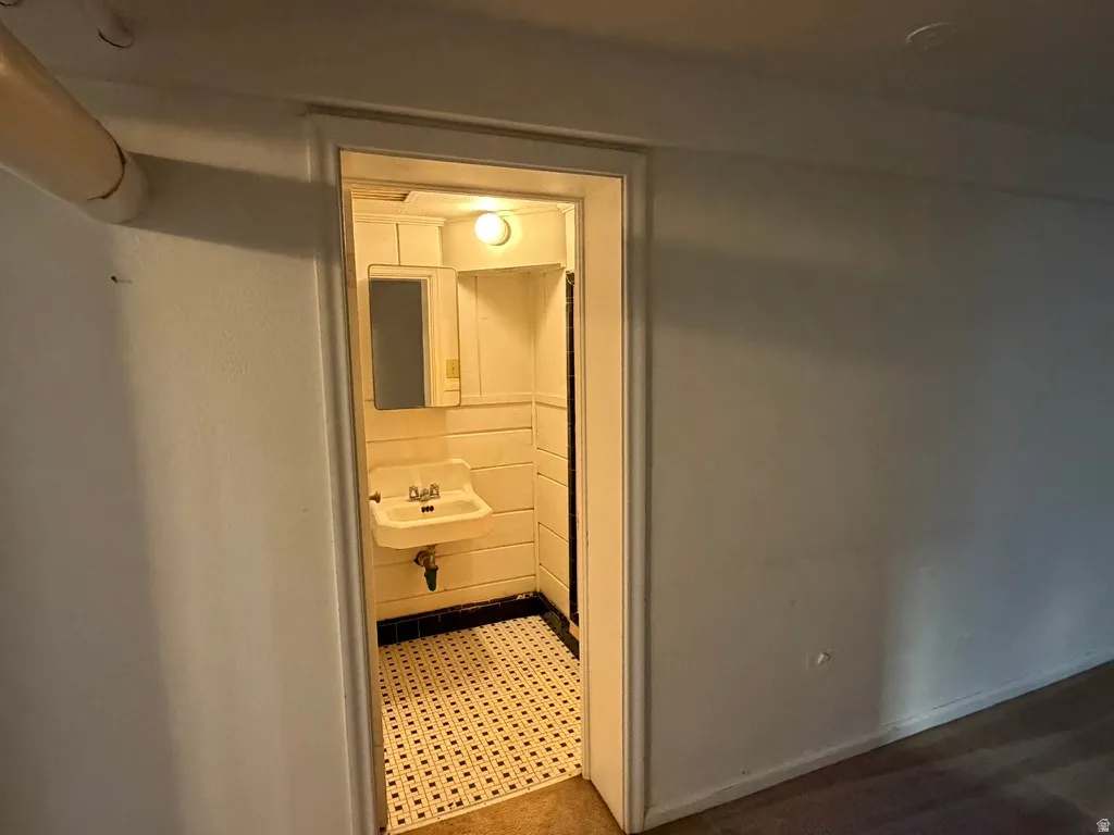 Wall-mounted sink with dual faucets, mirrored medicine cabinet, and patterned tile flooring