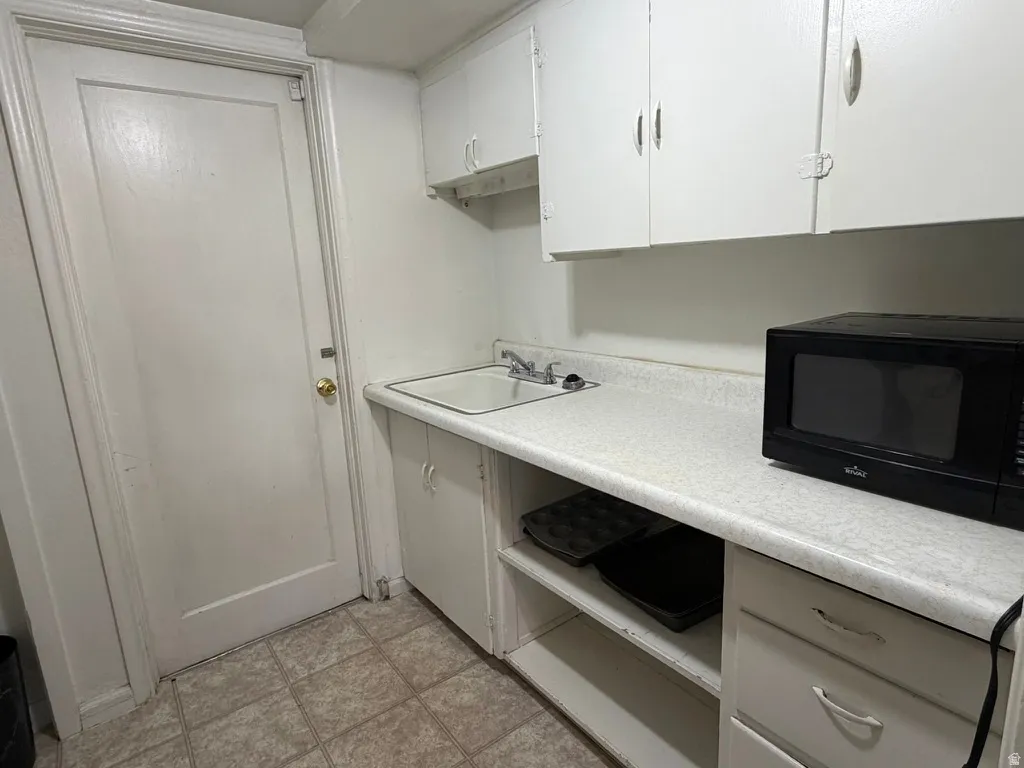 White cabinetry, laminate countertop, single basin sink with faucet, and tile flooring