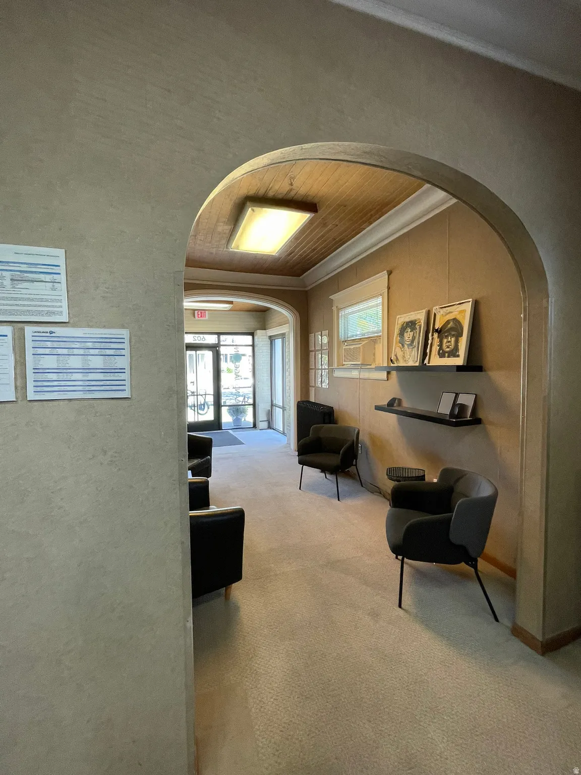 Corridor with arched walkways, wood ceiling, light colored carpet, crown molding, and a textured wall