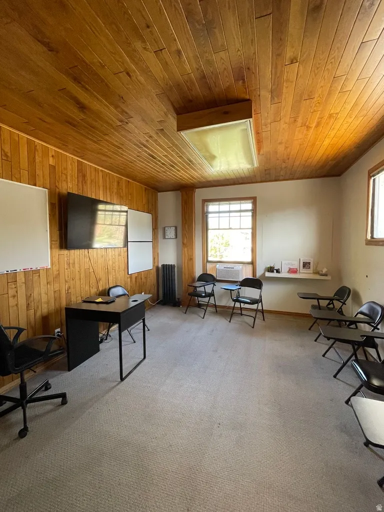 Office area featuring light colored carpet, radiator, wooden ceiling, and wood walls