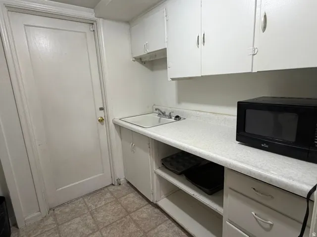 White cabinetry, laminate countertop, single basin sink with faucet, and tile flooring