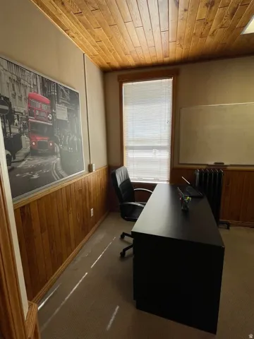 Carpeted office with wooden walls, wainscoting, wooden ceiling, and radiator