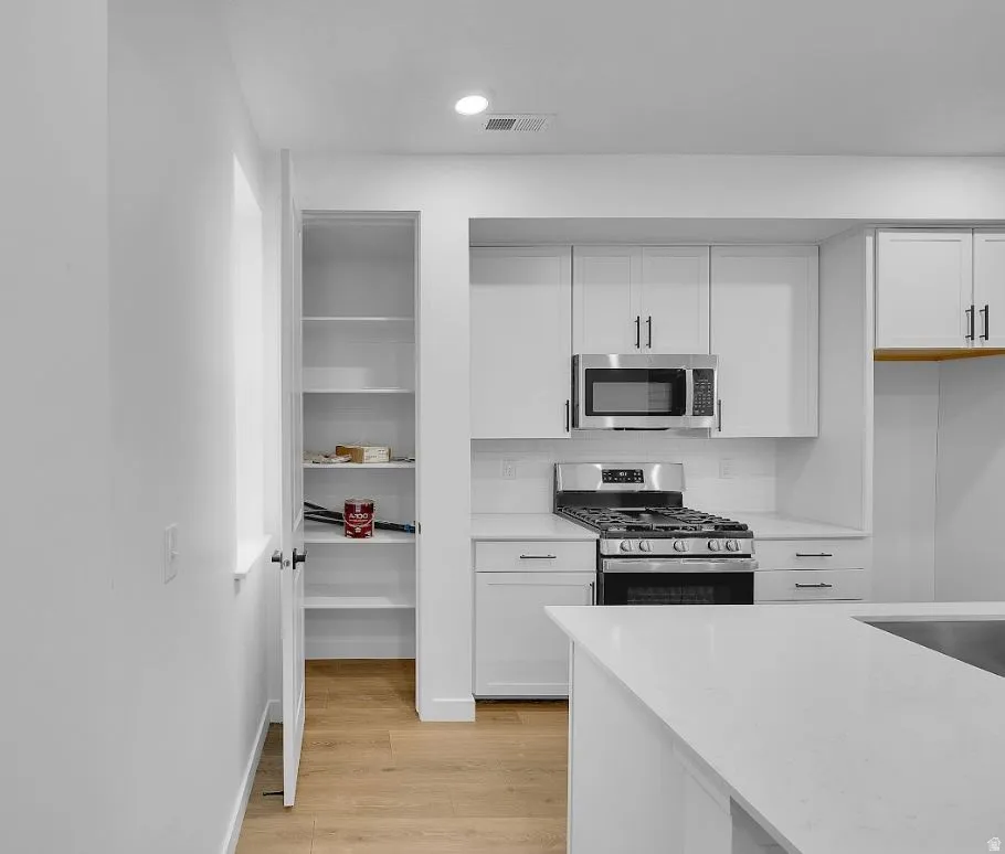 Kitchen featuring stainless steel appliances, white cabinets, light wood-style flooring, and recessed lighting