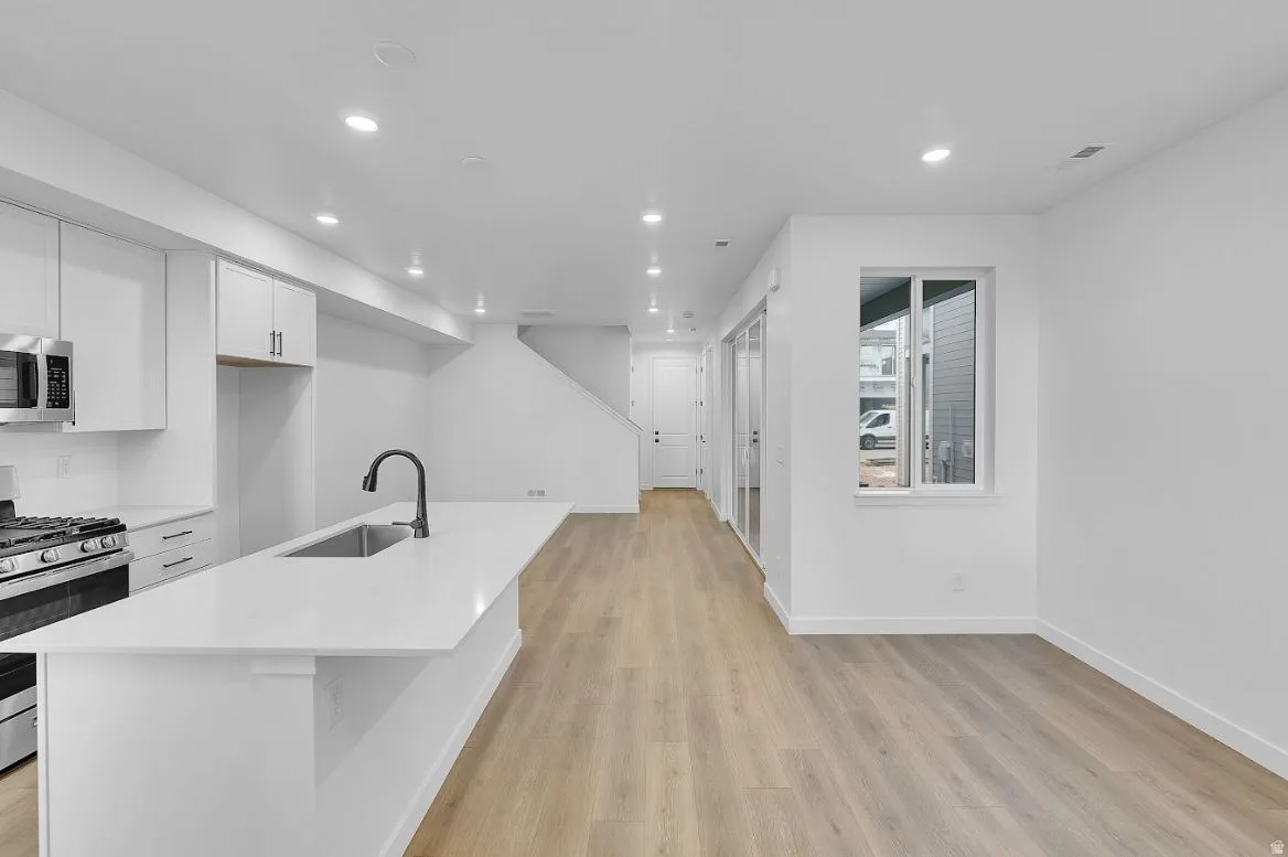 Kitchen with white cabinets, stainless steel appliances, recessed lighting, light wood-style flooring, and a center island with sink