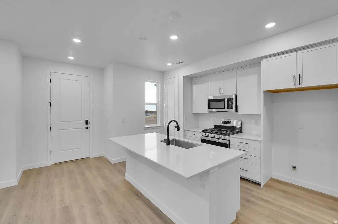 Kitchen with white cabinetry, stainless steel appliances, recessed lighting, a kitchen island with sink, and light wood-type flooring