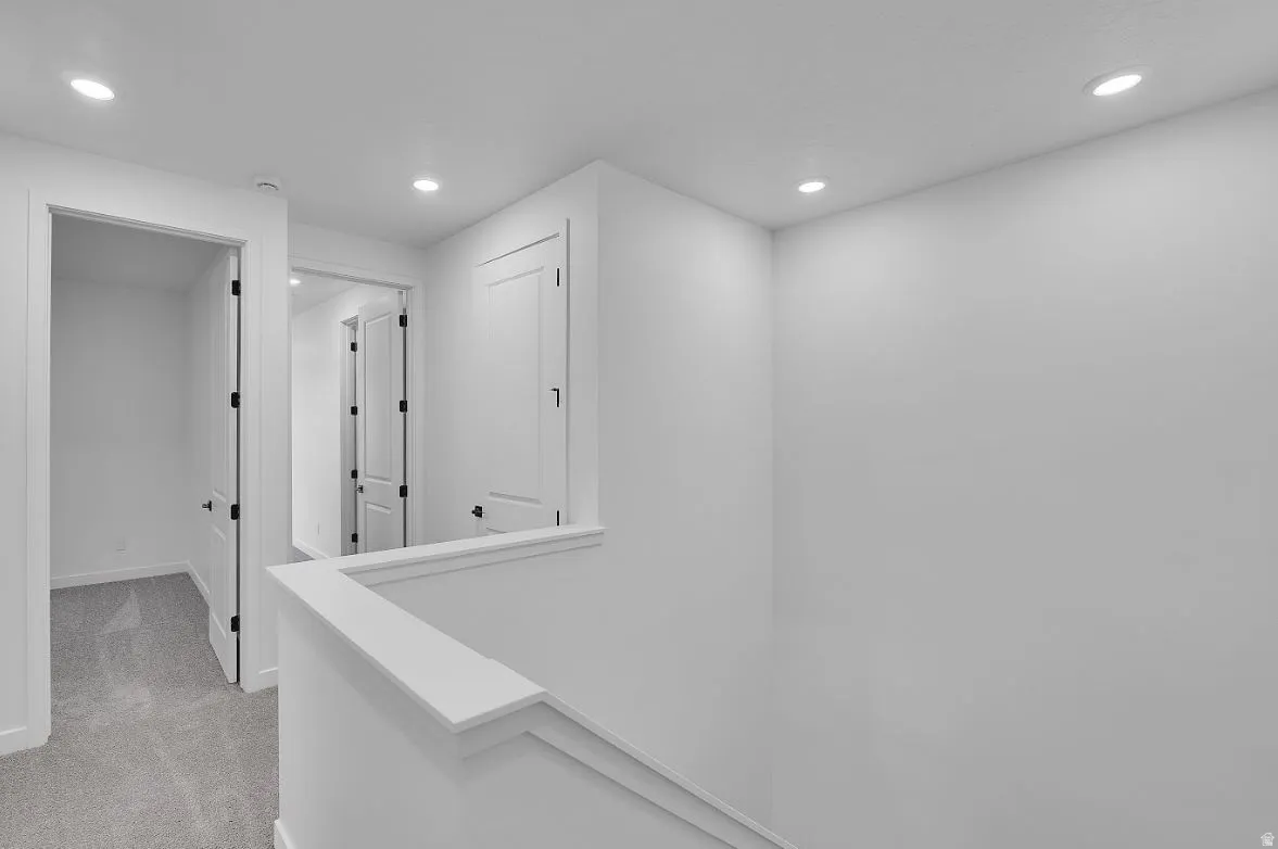 Hall with light colored carpet, recessed lighting, and an upstairs landing