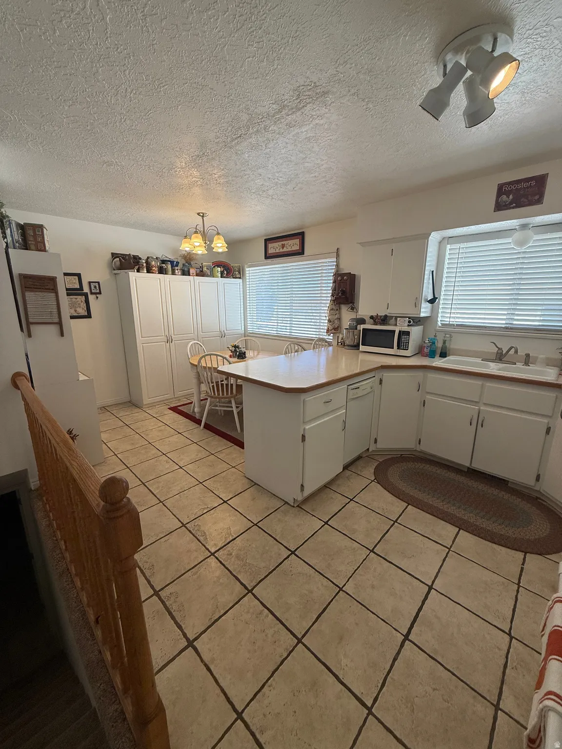 Kitchen featuring a peninsula, light countertops, white cabinets, a textured ceiling, and white appliances