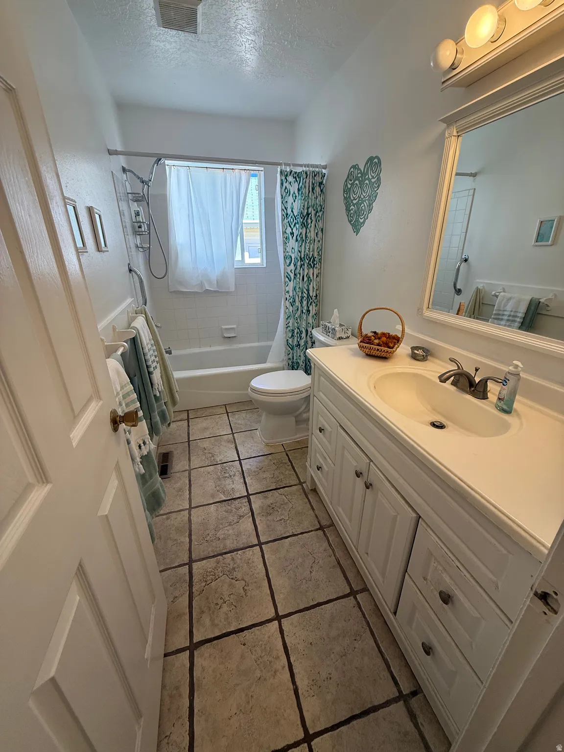Full bathroom with vanity, shower / bath combo with shower curtain, and a textured ceiling