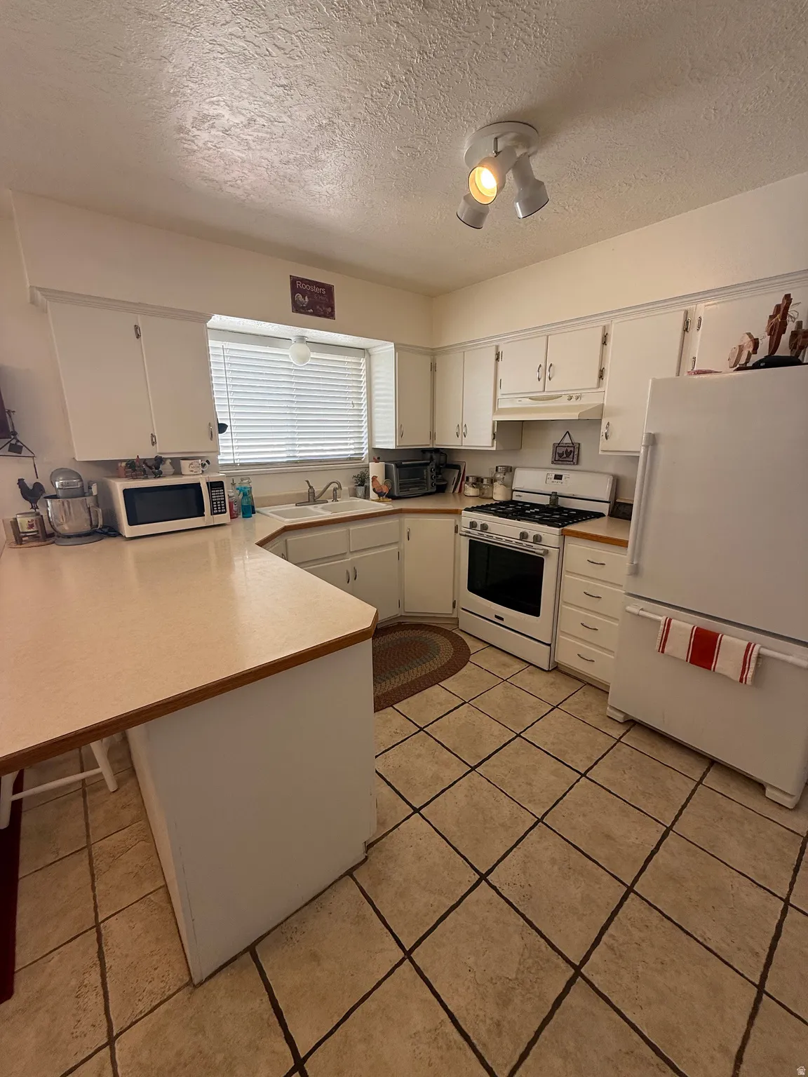 Kitchen with white appliances, a peninsula, white cabinets, light countertops, and a breakfast bar