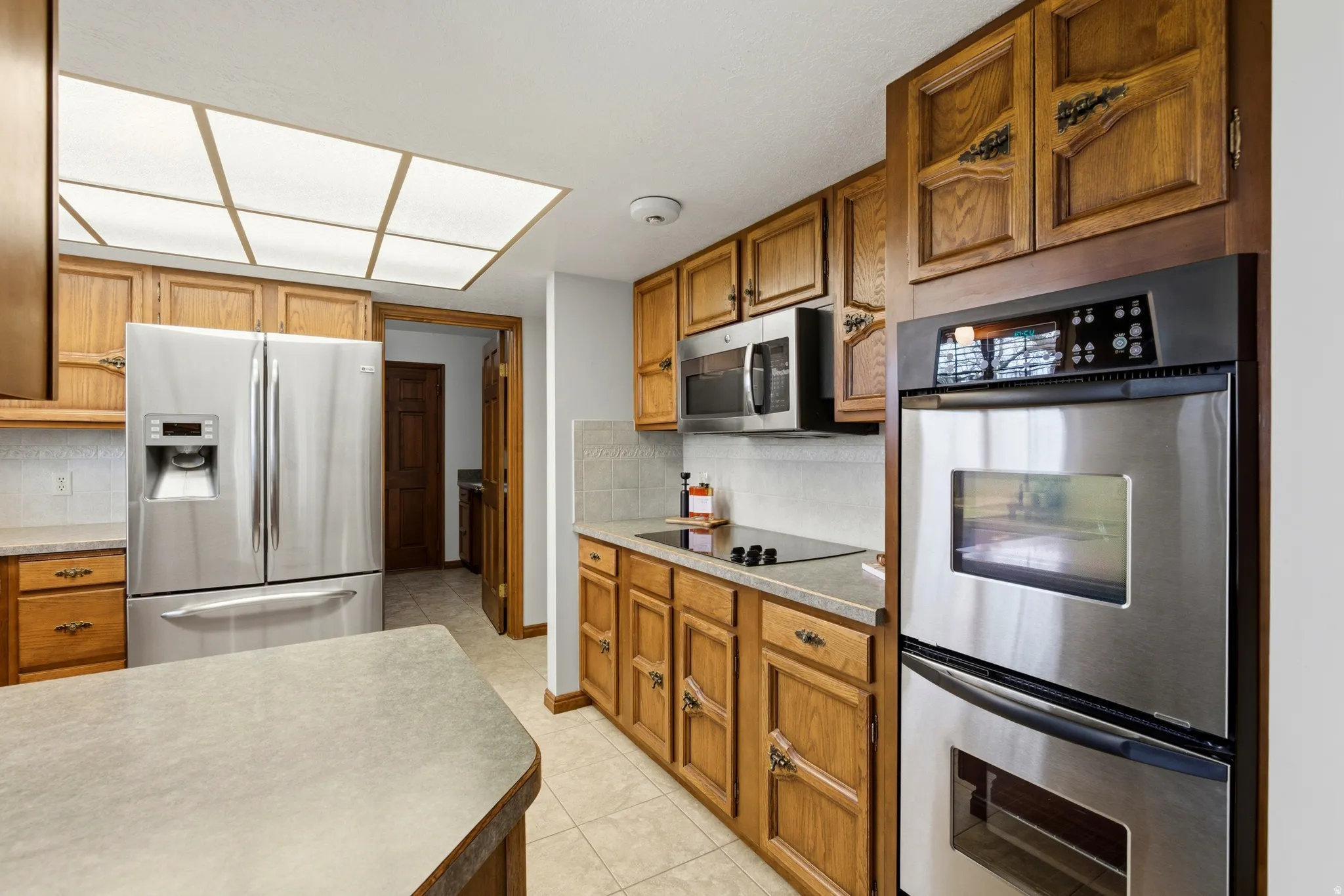 Kitchen with stainless steel appliances, wood finish cabinets, backsplash, and light countertops
